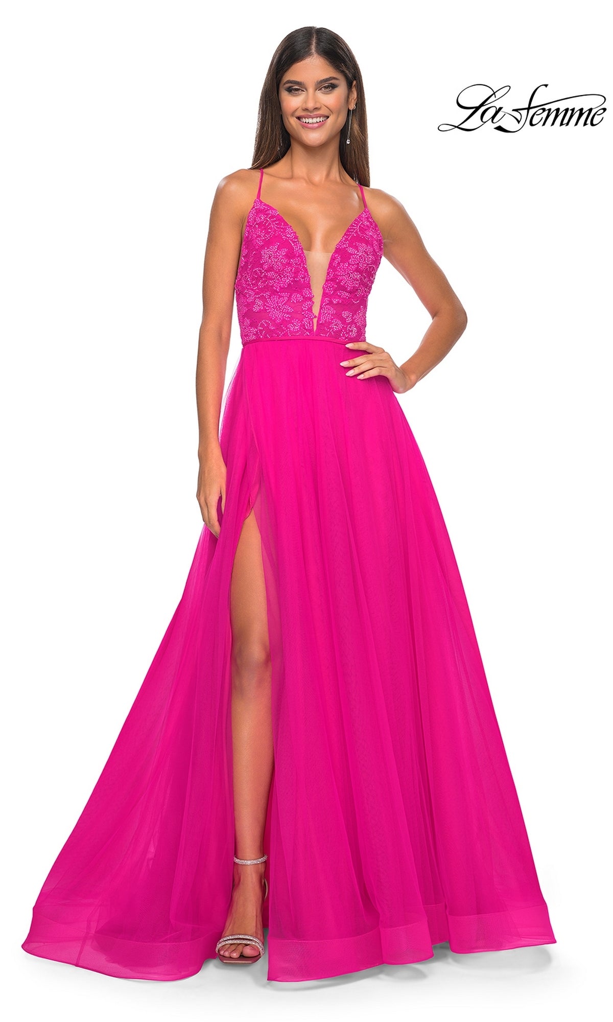 A woman wears the La Femme Deep V-Neck Long Tulle Prom Gown 32059, featuring a bright pink lace bodice, high slit, deep V-neckline, and long tulle skirt with strappy heels. The La Femme logo appears in the top right corner.